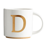 Taza COLLECTIVE HOME con monograma oro frontal, ideal para café matutino.