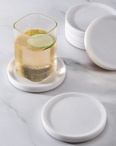 CHISELED ST DF SK posavasos de mármol blanco con borde elevado protegiendo la mesa.