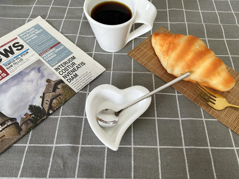 Descanso blanco con cuchara plateada junto a la cafetera.